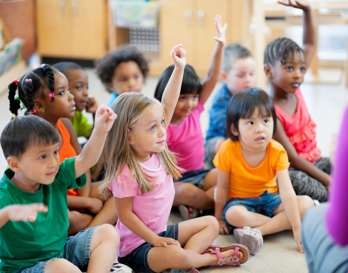 group of young children raising their hand in classroom