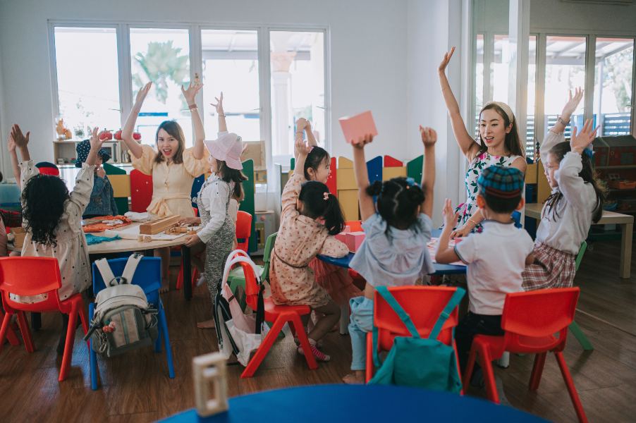 A group of children in Laurel, NJ, enthusiastically raises their hands at a table
