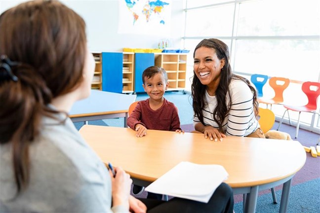 A preschool teacher talking with a mother and her child seated at a table