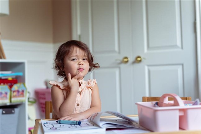 A young girl sitting at a table with a thoughtful expression